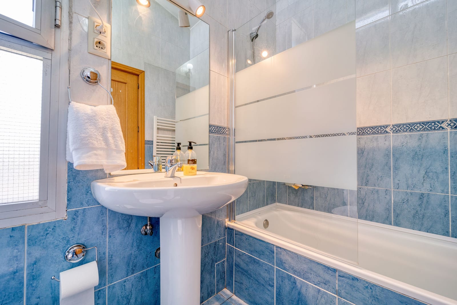 A tidy tiled student bathroom with a sink, folded towel and bathtub
