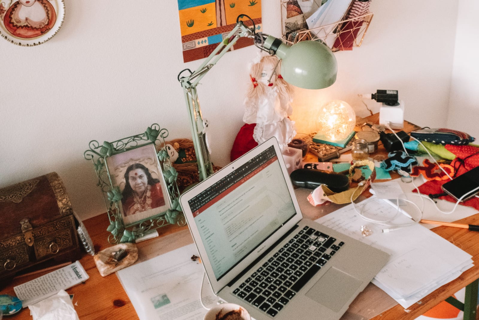 A student laptop open on a cluttered wooden study desk with a lamp, framed photo and coffee